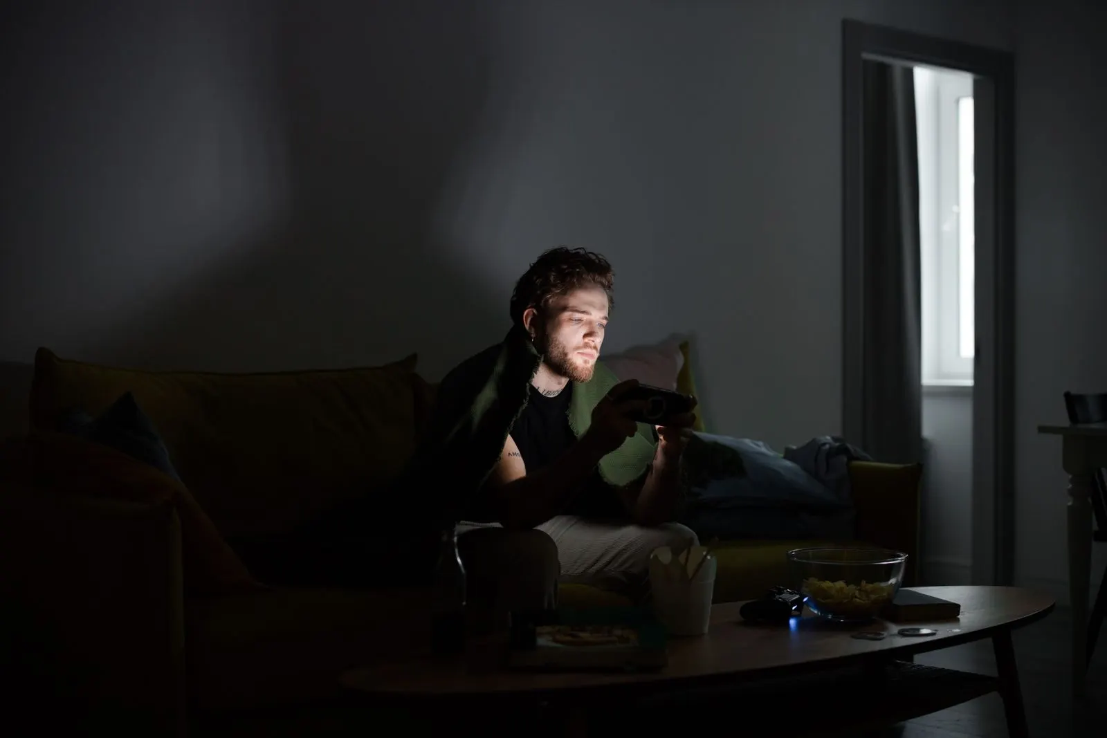 Ein junger Mann sitzt allein in einem abgedunkelten Raum und spielt konzentriert am Handy, das Display beleuchtet sein Gesicht