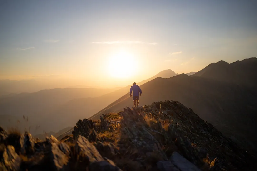 Eine Gestalt steht bei Sonnenaufgang auf einem Berggipfel