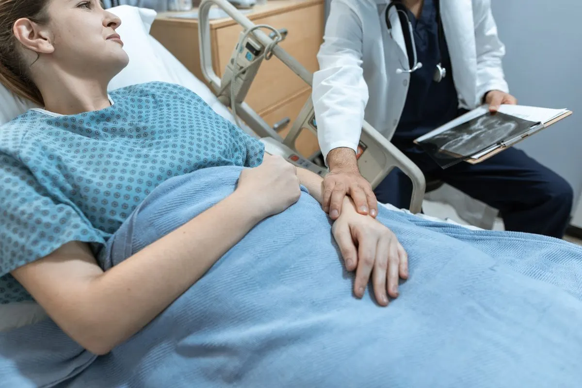 Eine Ärztin sitzt am Krankenbett, eine Hand auf der Hand der Patientin, während diese angespannt zuhört