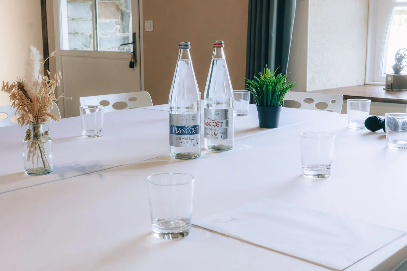 Ein gedeckter Besprechungstisch mit Wassergläsern, Flaschen und einem Mikrofon, bereit für eine Verhandlung