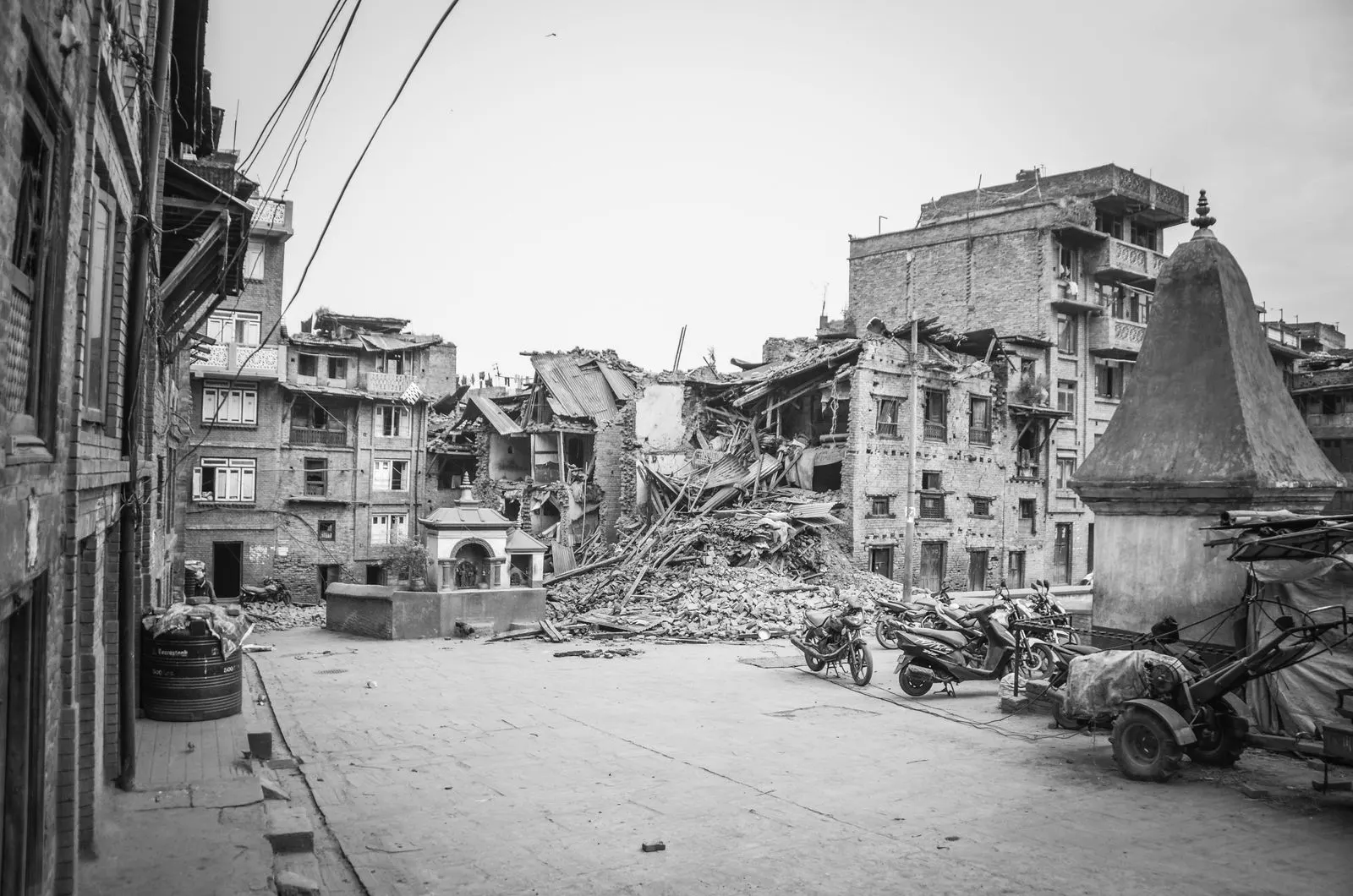Eingestürzte Häuser und Trümmerberge in Bhaktapur nach dem Erdbeben, eine leere Straße mit geparkten Motorrädern, in Schwarzweiß