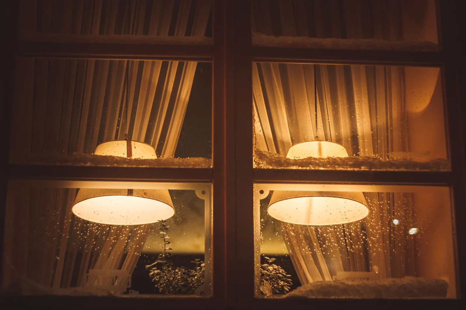 Warmes Lampenlicht durch ein schneebedecktes Fenster, von draußen in der winterlichen Dunkelheit gesehen